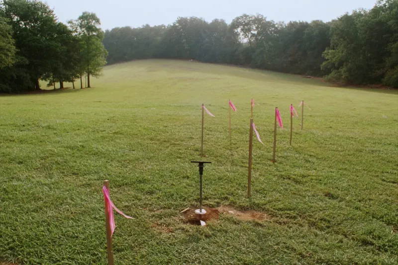 Survey stakes with pink flagging and a soil auger in a boring hole on a North Alabama pasture