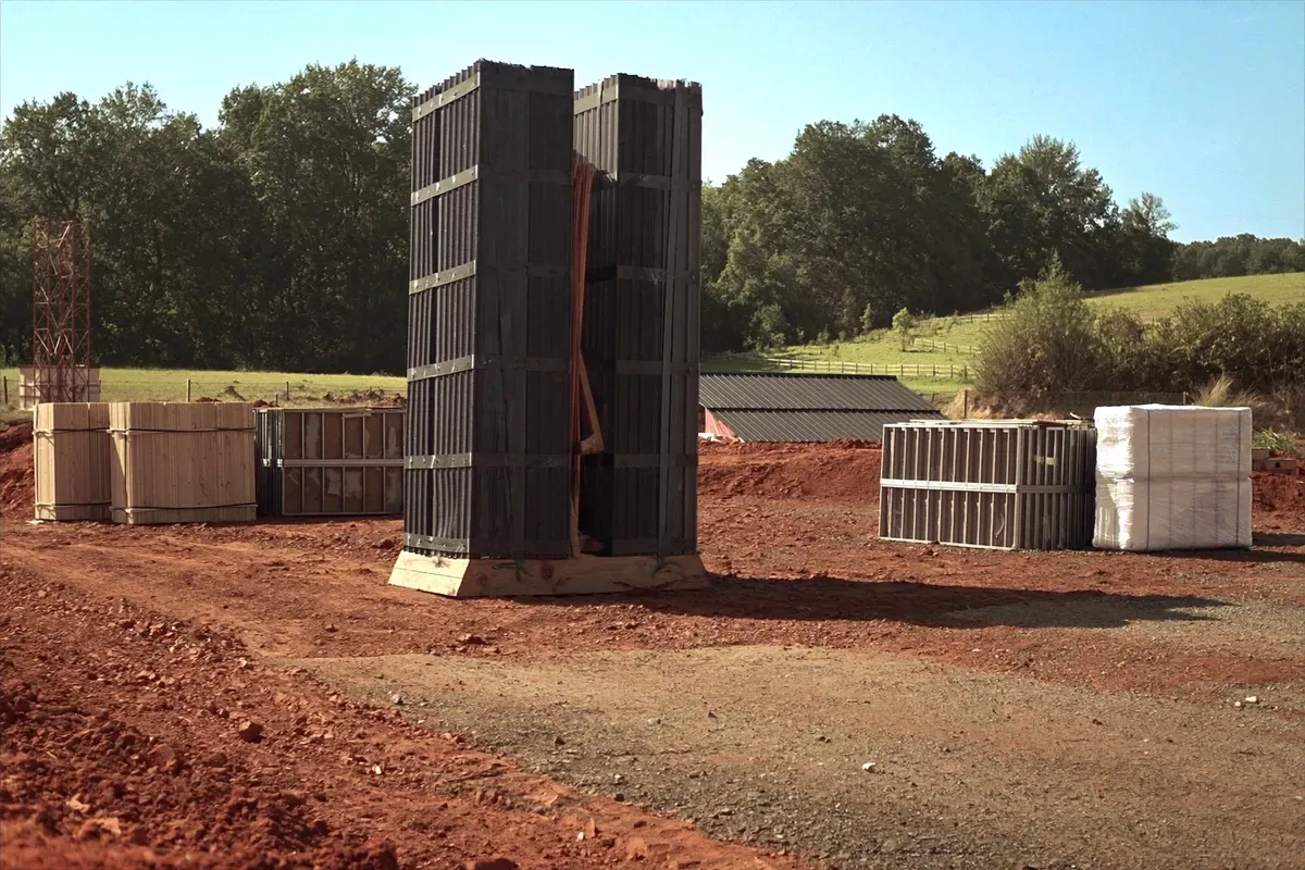 Metal roofing panels, lumber and wrapped insulation staged on a red clay pad in North Alabama