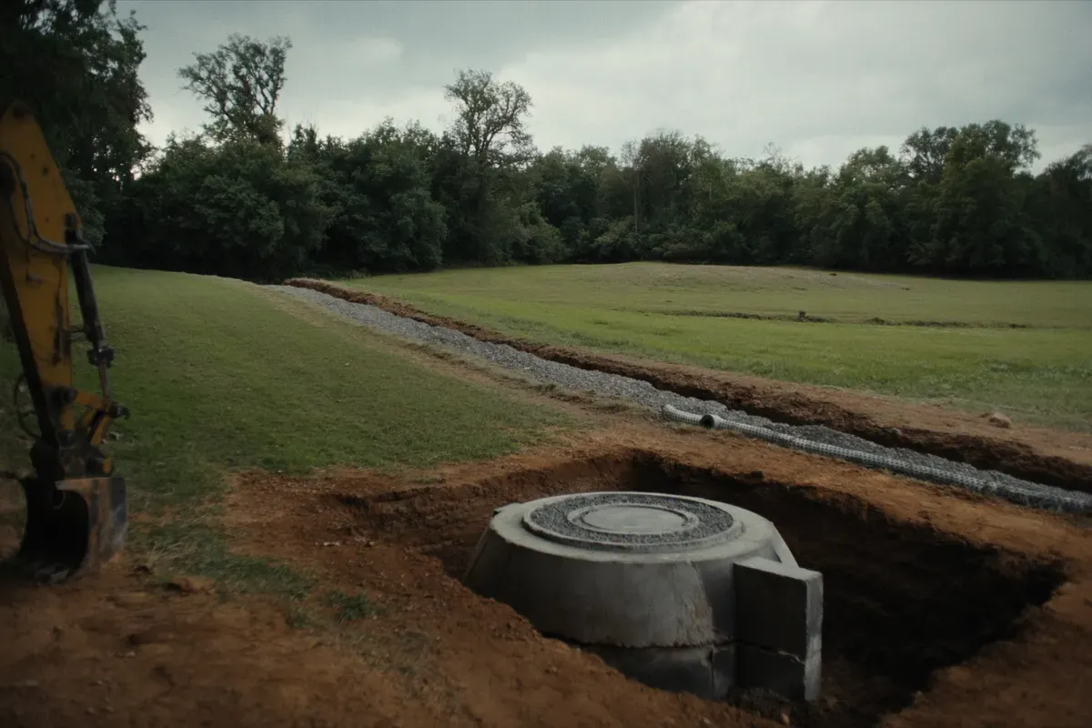 Precast septic tank set in an excavation with a gravel drain field trench on a rural Alabama lot