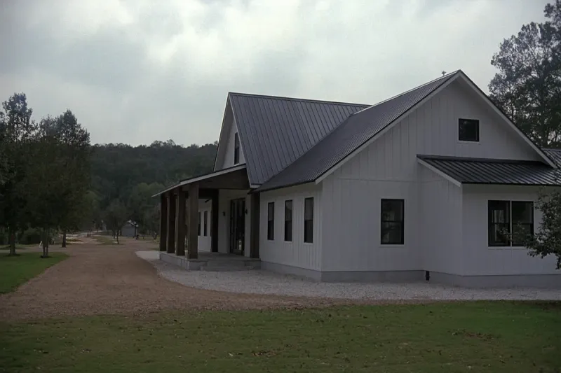 Finished white board-and-batten post-frame barndominium with a charcoal metal roof and covered porch in North Alabama